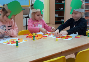 Dzieci przyklejają na konturach drzew "liście": żółte i czerwone kawałki papieru.
